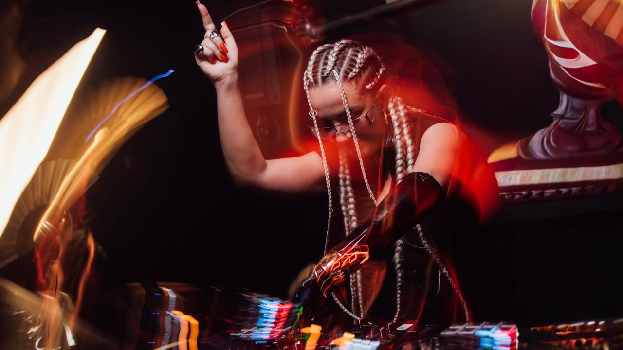 KSU behind the decks at PROMIN', arm raised, in streaks of red light